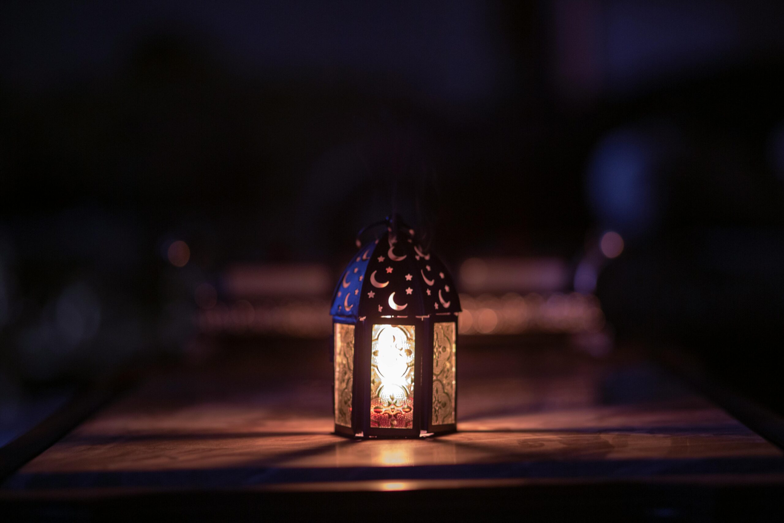 A beautifully decorated lantern illuminates a dark room, symbolizing Ramadan.